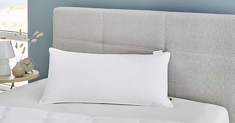 Close-up of a gray textured headboard with a white lumbar pillow on a bed with white bedding. Partial view of nightstand with decor.