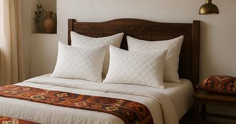Bedroom with wooden headboard, white bedding, and colorful patterned runner. Wall niche with vase, brass pendant light. Warm, inviting atmosphere with earthy tones and textures.
