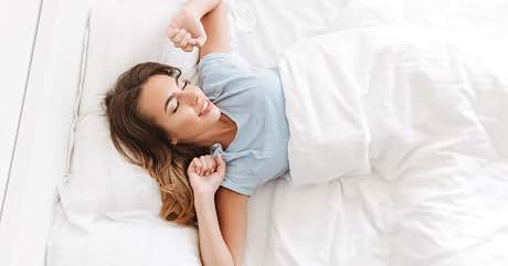 a woman lying in bed with her hands in her mouth.